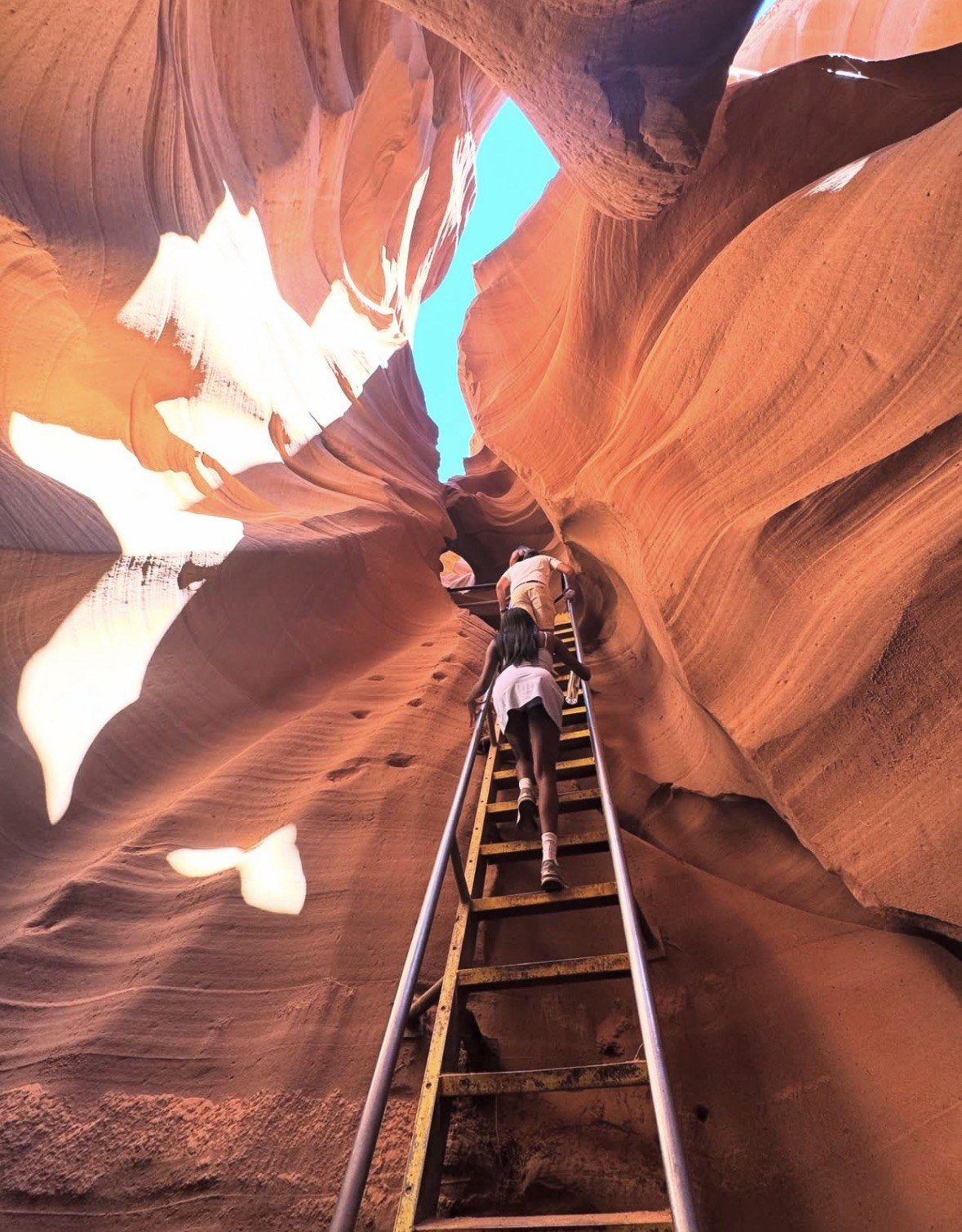 Two visitors climbing a wooden ladder toward blue sky above