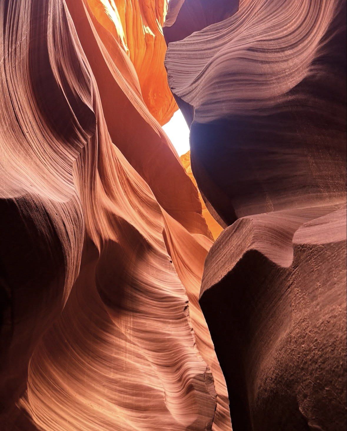 Flowing sandstone ribbons rising toward a glowing gap of daylight