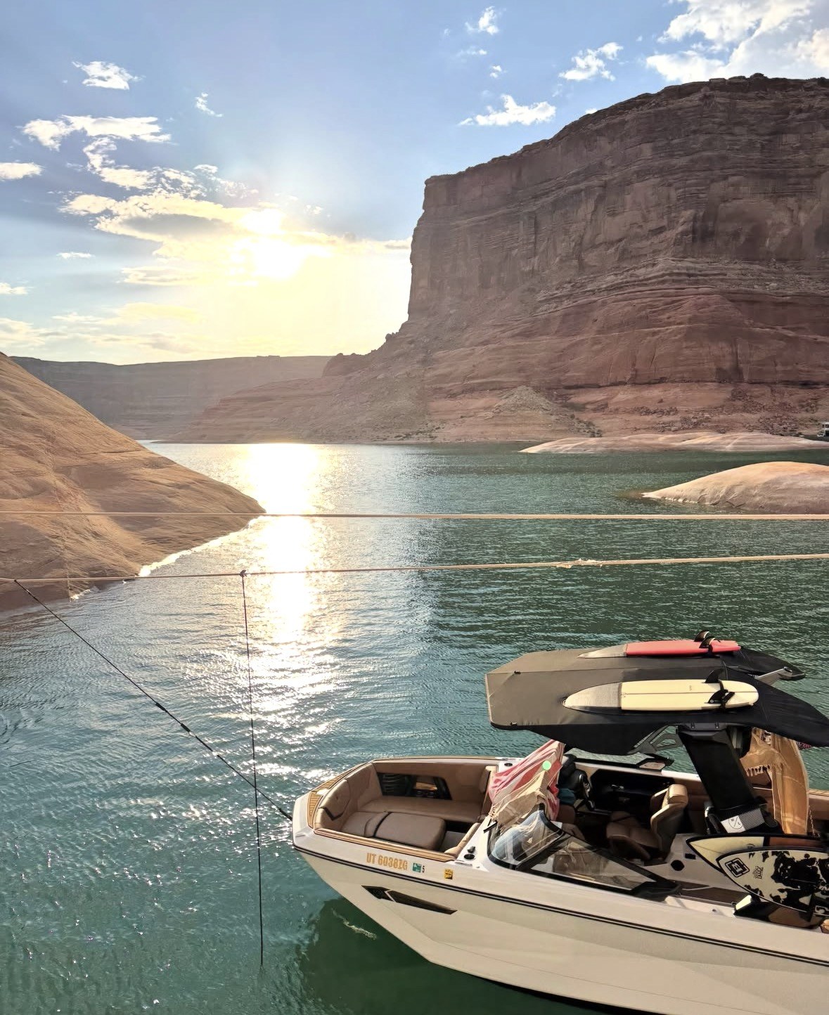 Boat moored under a tall sandstone wall on Lake Powell in late sun