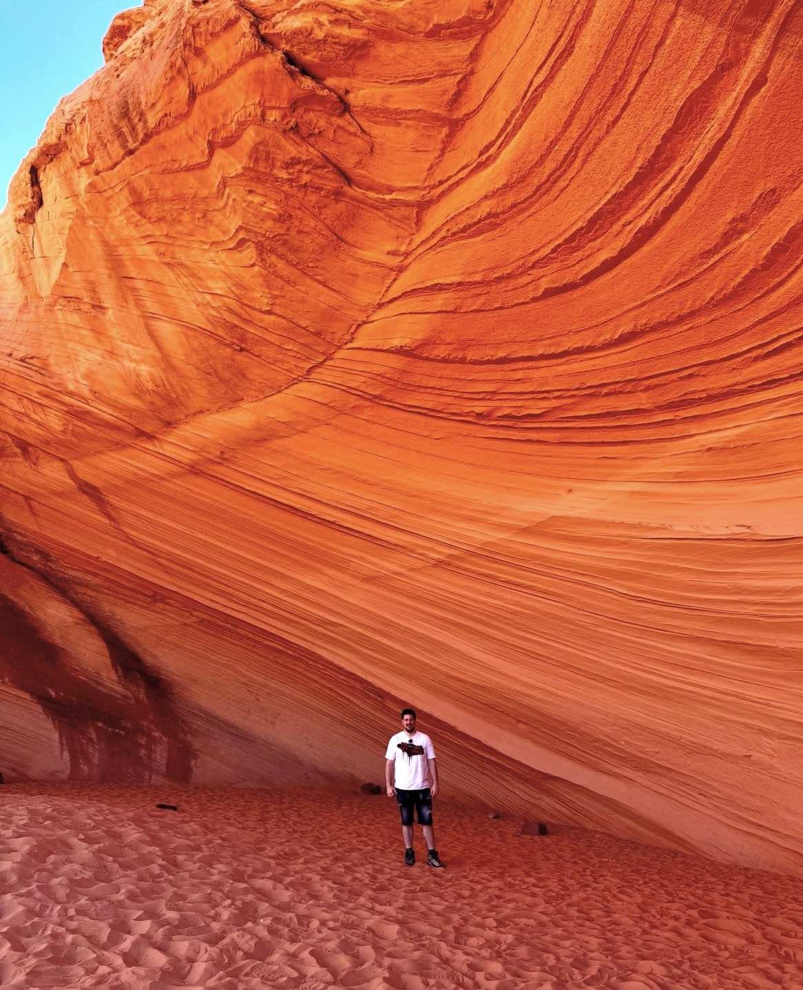 Visitor dwarfed by a red sandstone alcove with wave-like layers