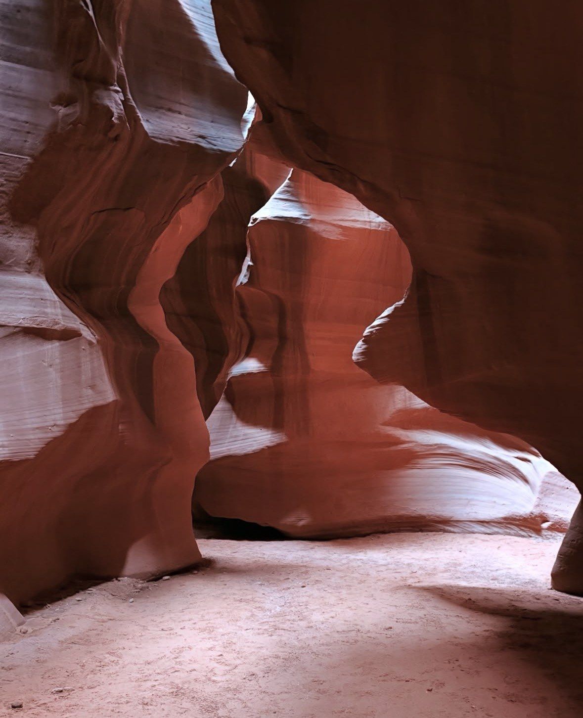 Pale sandy floor winding between smooth red walls in soft light