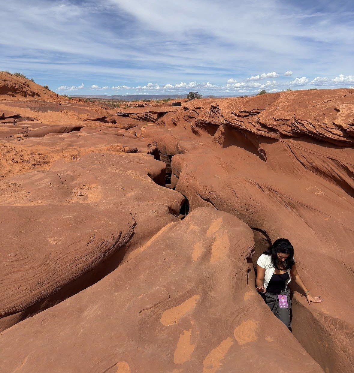 Woman emerging from the slot entrance onto open red rock plateau