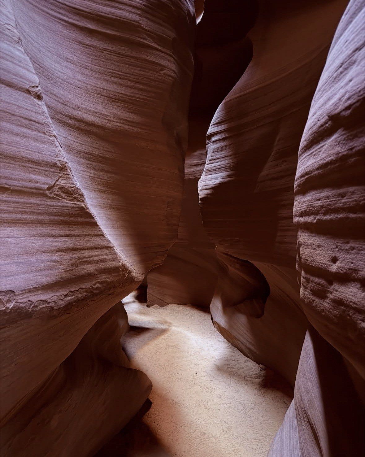 Winding shadowed corridor with a sunlit sand path through Antelope Canyon