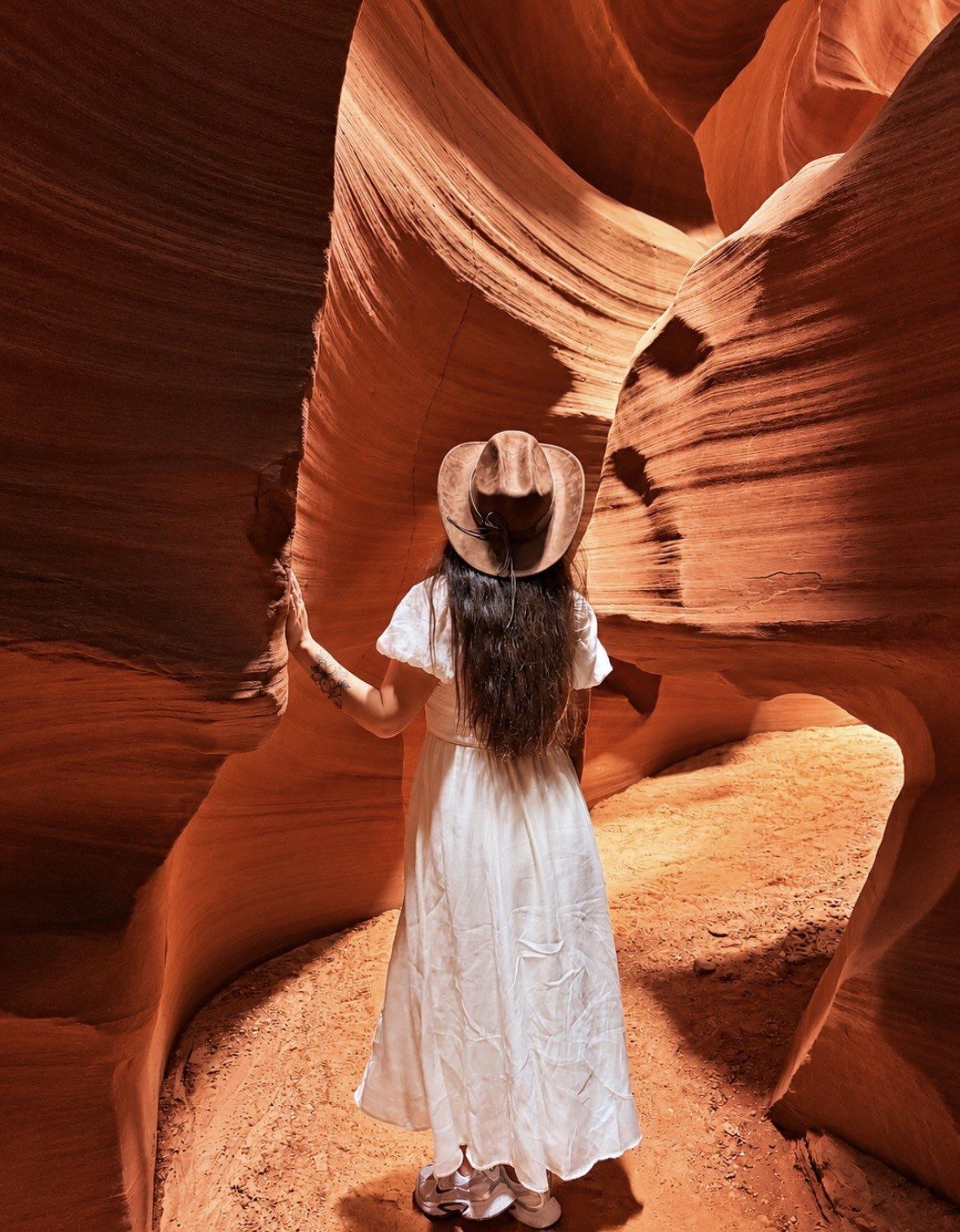 Woman in white dress and straw hat walking the sandy canyon floor
